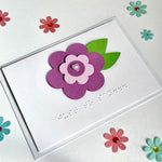 Flower just to say card on a white background. The card is surrounded by pink and blue paper flowers.