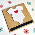 New baby card on a white back ground. The card is surrounded by the pink and blue paper flowers.